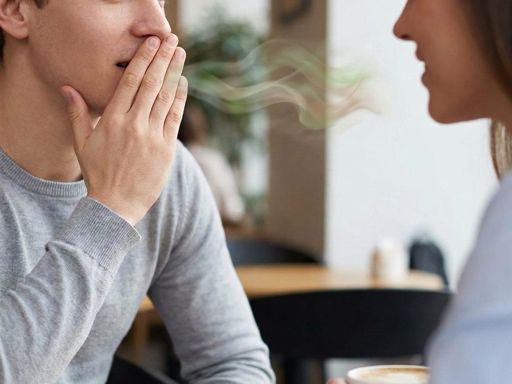 Persona que se tapa la boca por mal aliento durante una conversación